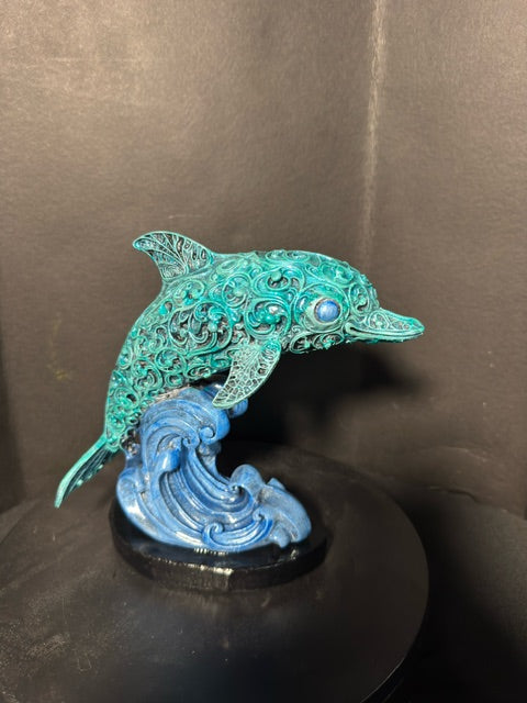 Filigree dolphin statue front view — teal lacework body cresting a cobalt wave