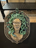 Front view of Medusa relief with green serpents and ornate skull-accented frame