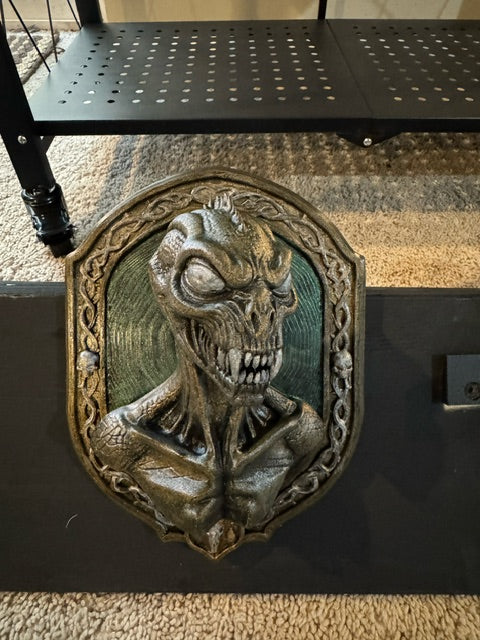 Front view of bronze-toned Chupacabra relief with teal backdrop and ornate skull-accented frame